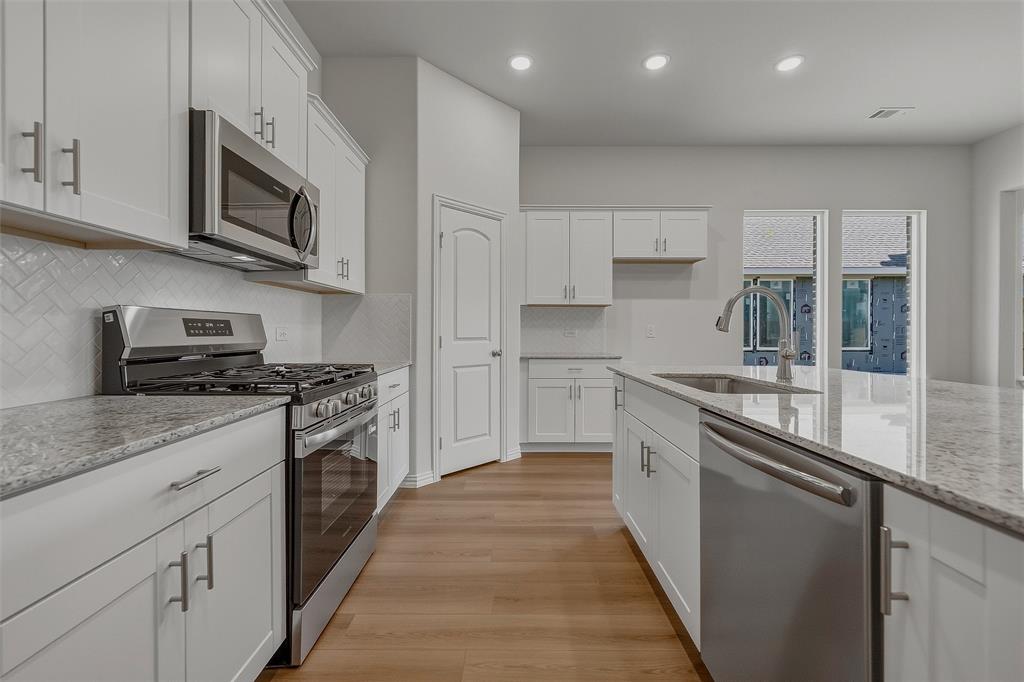 Modern kitchen featuring white cabinetry, stainless steel appliances, granite countertops, wood-finish flooring, and a herringbone tile backsplash