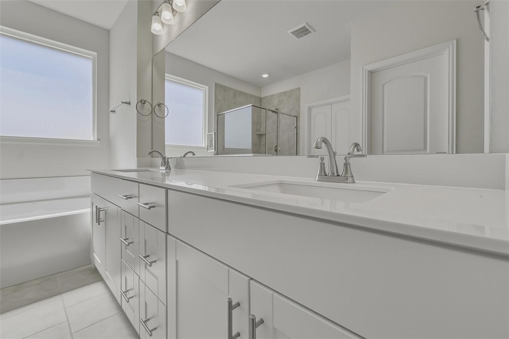 Dual vanity with white cabinetry and chrome hardware, integrated sinks, large mirrored wall, and built-in bathtub