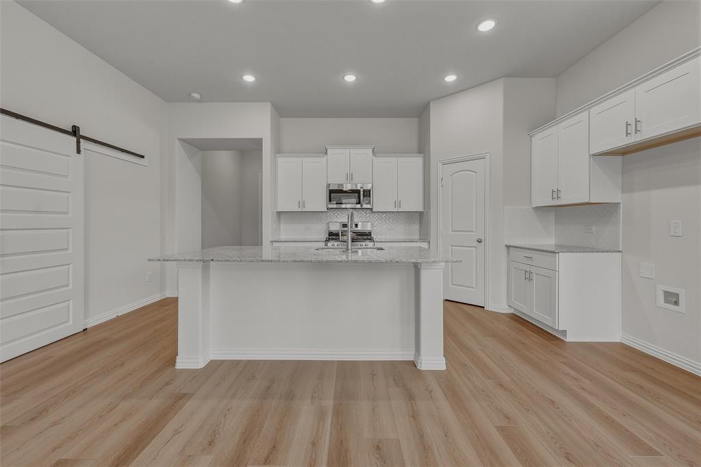 Kitchen featuring a central island with a light-toned countertop, white cabinetry with silver-toned hardware, stainless steel microwave, and wood-finish flooring