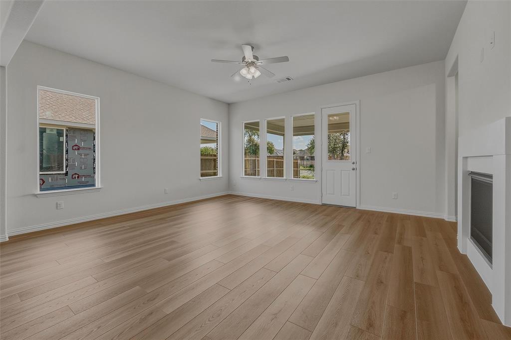 Spacious room featuring light wood-finish flooring, multiple windows, a ceiling fan, and a built-in fireplace