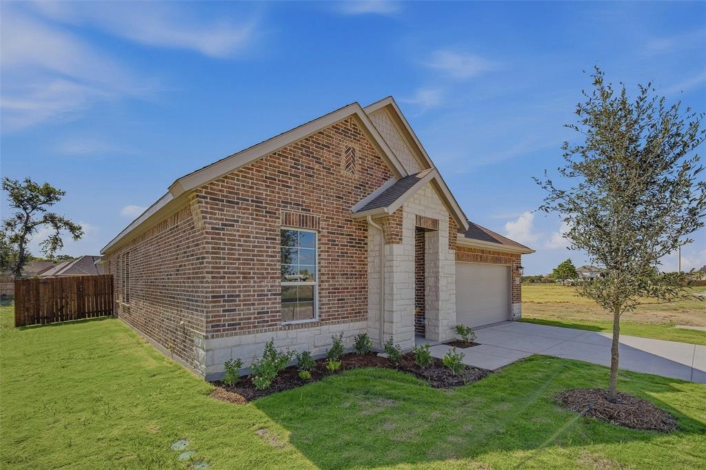 Brick exterior with stone accents, attached garage, concrete driveway, and manicured lawn