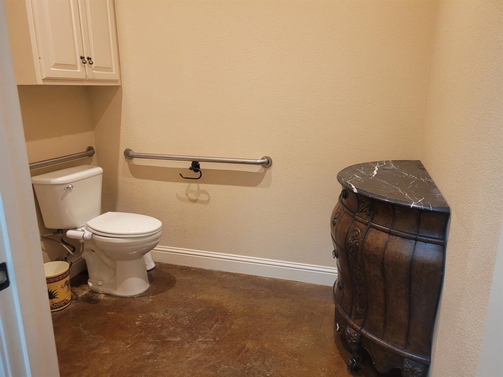 Bathroom featuring a white toilet, support bars, and built-in upper cabinetry with white doors and dark hardware