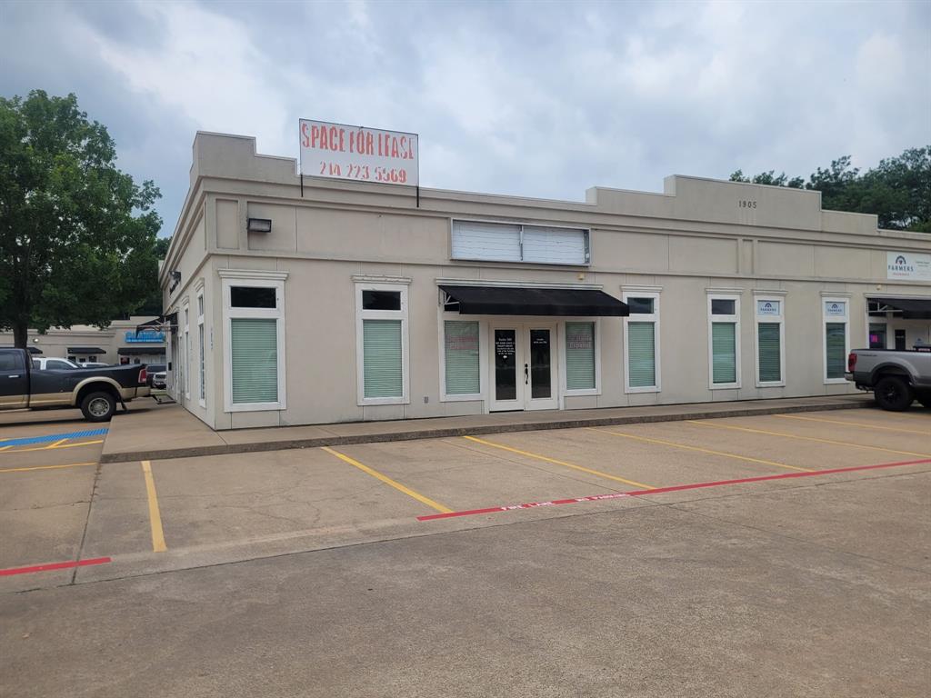 Commercial storefront featuring a recessed entry, prominent black awning, multiple display windows, and a dedicated concrete parking lot with painted space dividers