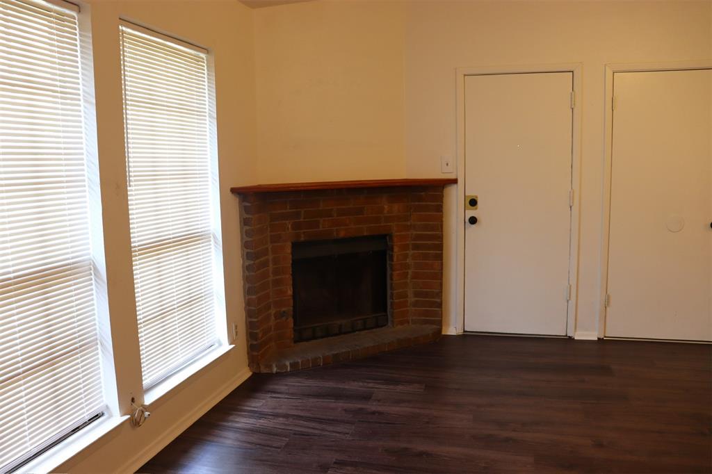 Living area featuring a corner brick fireplace with a wood mantel, dark wood-finish flooring, and two windows with blinds