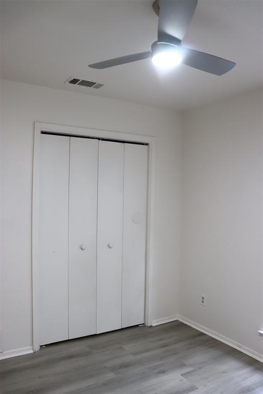 Room featuring wood-finish flooring, white walls, and a modern ceiling fan with integrated lighting