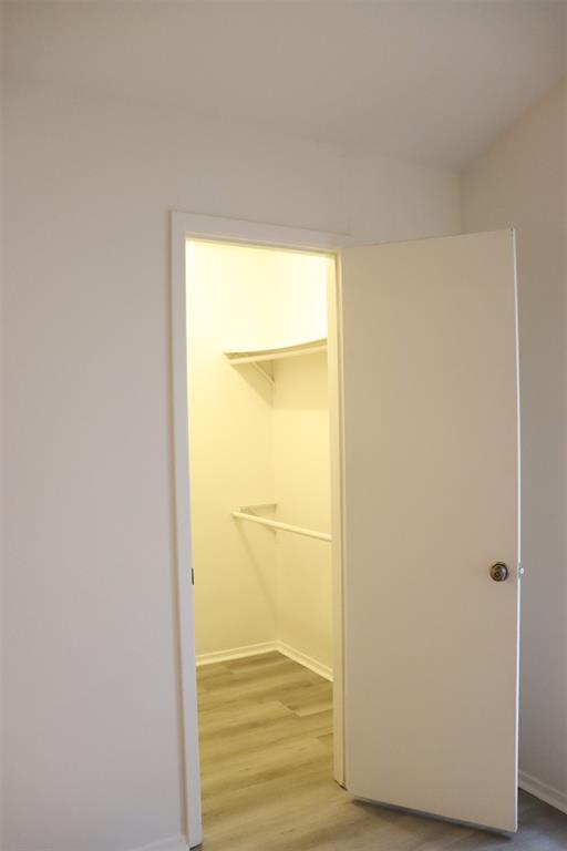 Interior closet featuring wood-finish flooring, white walls, and built-in shelving with a hanging rod