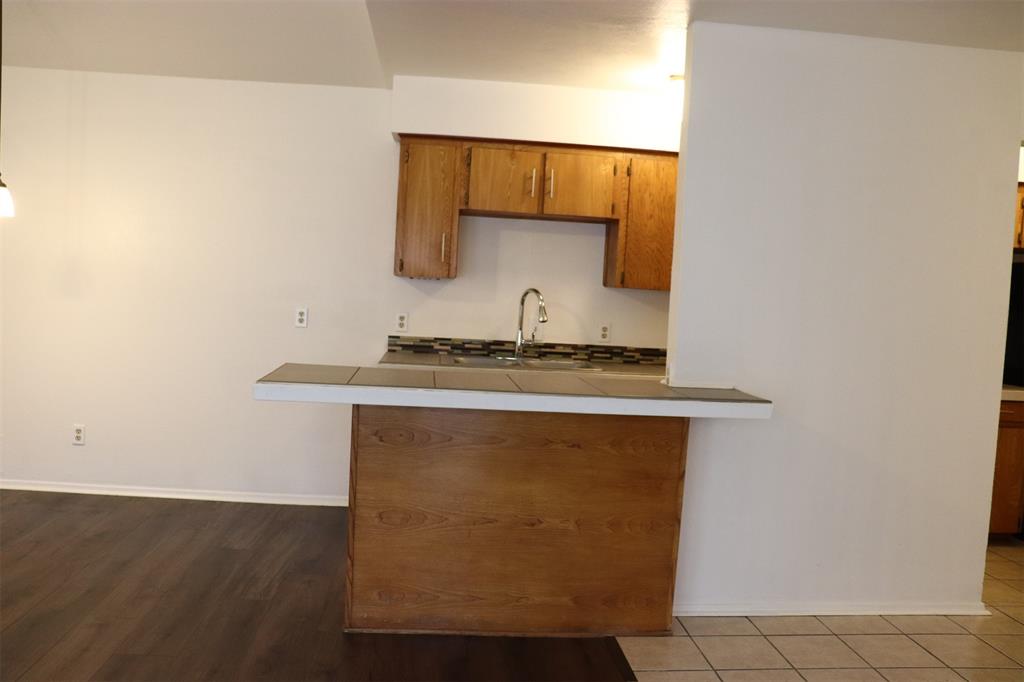 Kitchen featuring a breakfast bar with tile countertop, wood-finish cabinetry, stainless steel faucet, and tile backsplash