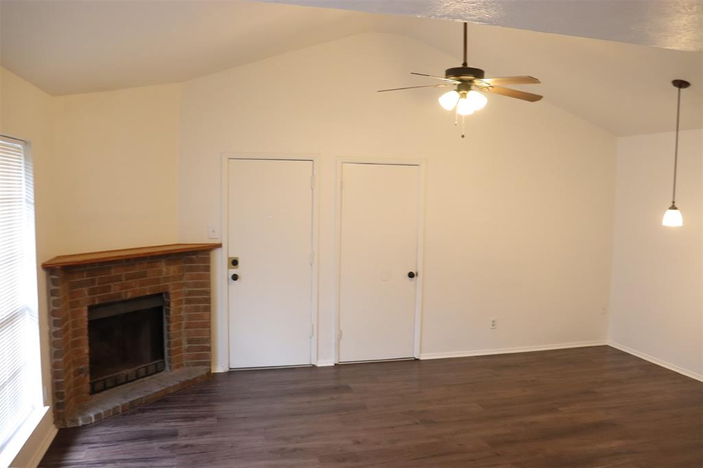 Living area featuring a brick fireplace with a wood mantel, wood-finish flooring, and a vaulted ceiling