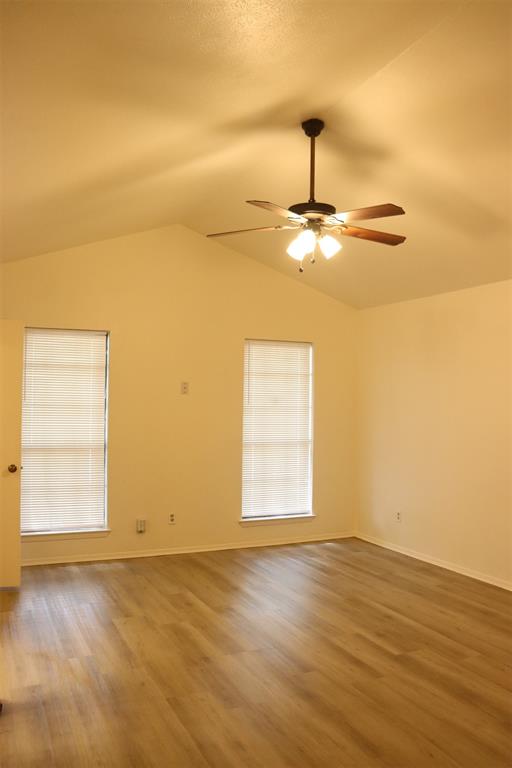 Spacious room featuring vaulted ceilings, wood-finish flooring, two large windows with blinds, and a ceiling fan with integrated lighting