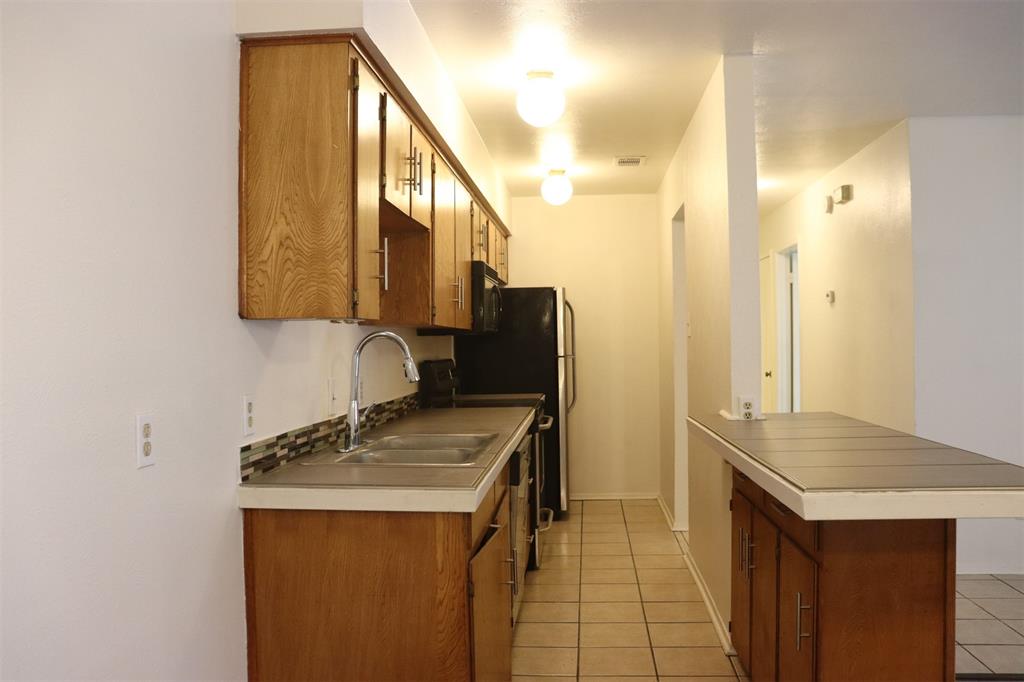 Galley kitchen featuring wood-finish cabinetry, tile flooring, and a double-basin stainless steel sink with a gooseneck faucet