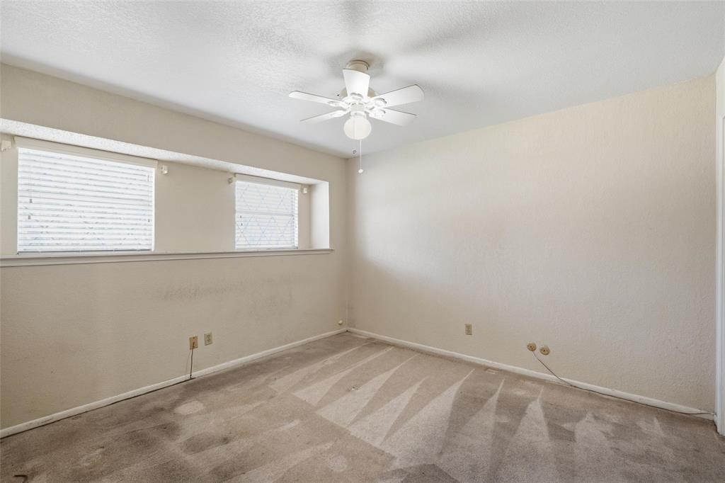 Carpeted room with a ceiling fan, two upper windows with blinds, and neutral-toned walls