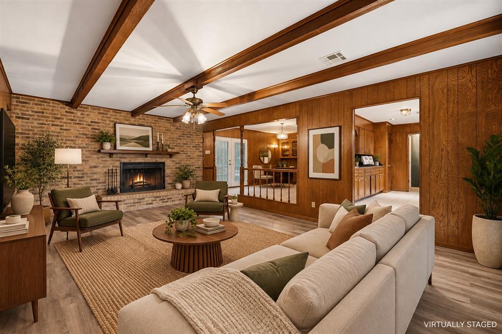 Exposed wood beam ceiling, brick fireplace with mantel, wood paneling, wood-finish flooring, and ceiling fan