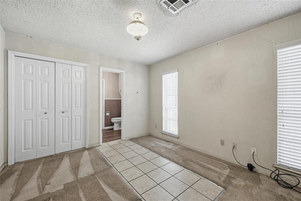 Carpeted room with a central tiled pathway, featuring bi-fold closet doors and multiple windows with horizontal blinds