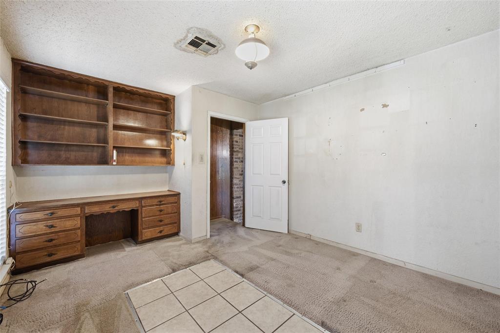Built-in wood-finish shelving and desk unit, white interior door, and mixed flooring with carpet and square tiles