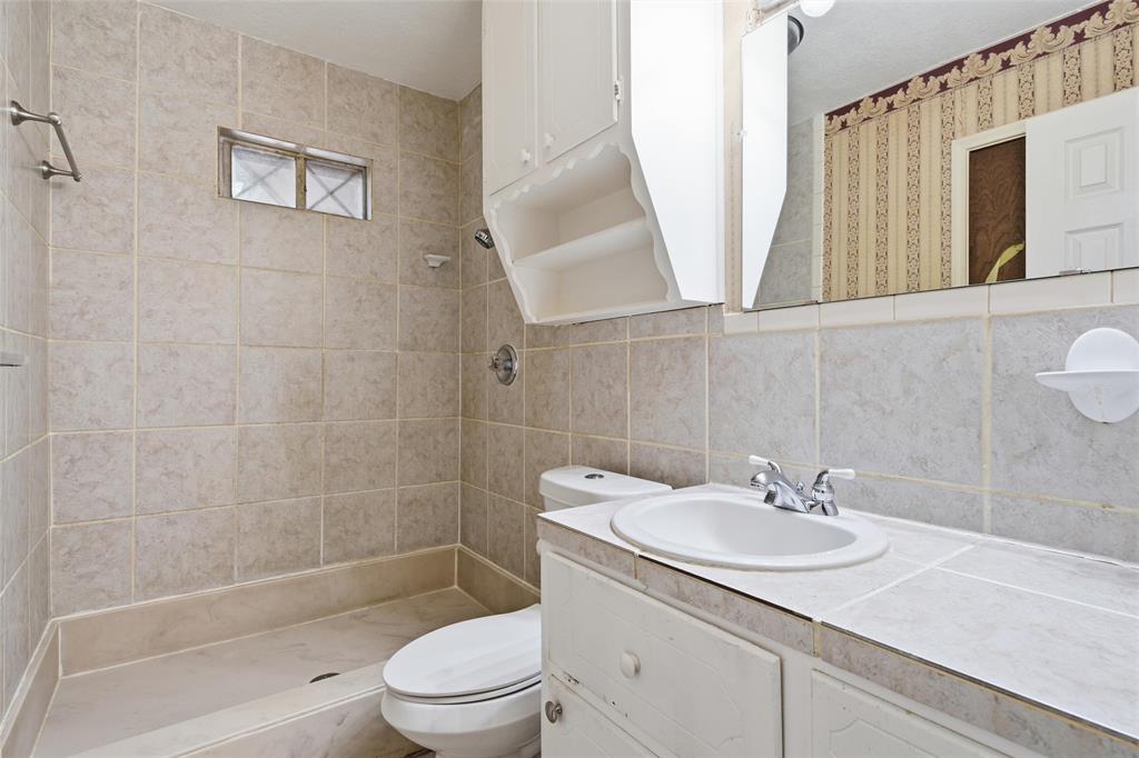 Bathroom featuring a tiled shower enclosure, white vanity with integrated sink, mounted mirror, and overhead storage cabinetry
