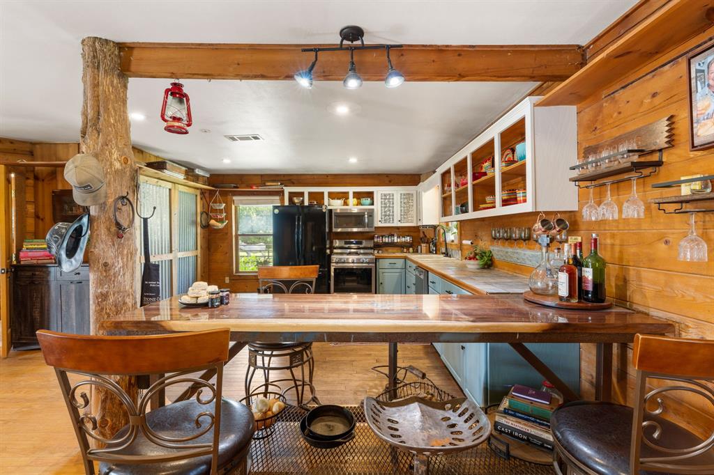 Kitchen featuring wood-paneled walls, a natural wood beam, track lighting, light blue lower cabinetry, white open upper shelving, and a dark wood-finish countertop