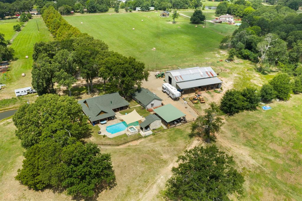Expansive property featuring a main residence with a swimming pool, detached covered patio, a large barn, and surrounding green acreage