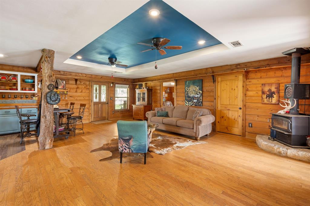 Spacious living area featuring wood-finish flooring, wood-paneled walls, and a recessed ceiling with a blue accent panel