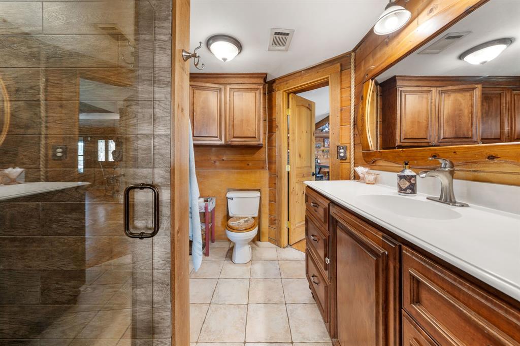Bathroom featuring a clear glass shower enclosure, wood-paneled walls, a single vanity with a white countertop and dark wood cabinetry, and tiled flooring