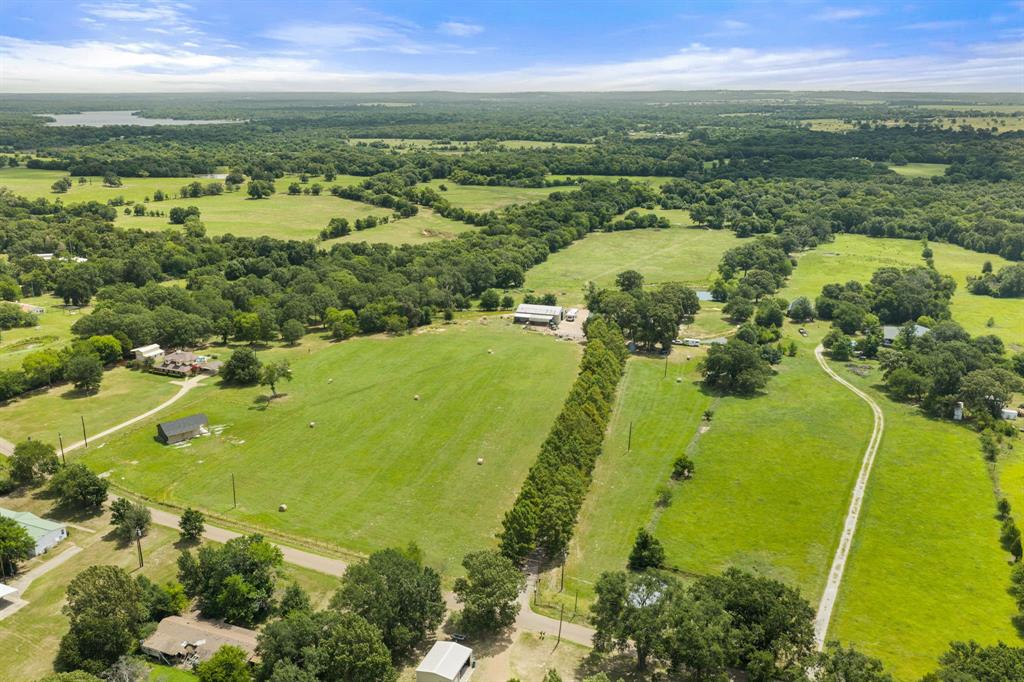 Expansive rural landscape featuring lush green fields, scattered mature trees, and a distant body of water