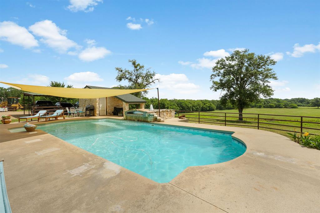 Outdoor pool with expansive concrete decking, stone-clad outdoor kitchen structure, and a secondary spa feature