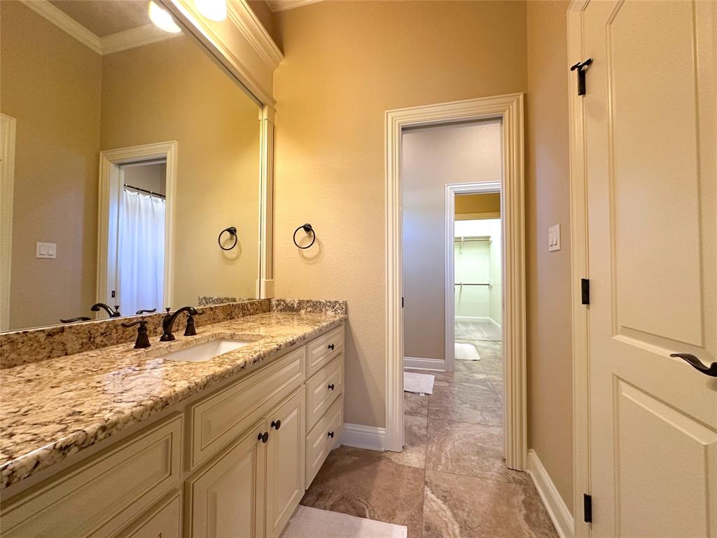 Bathroom vanity featuring a light-toned stone countertop, dual-basin sink, and dark bronze fixtures