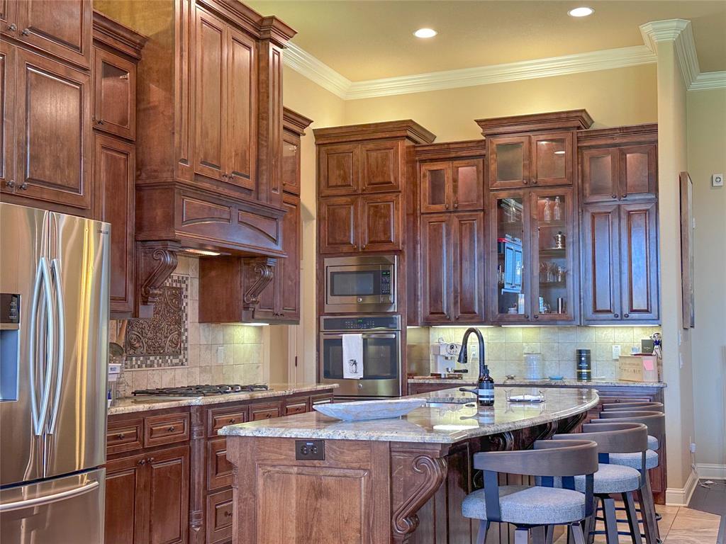 Gourmet kitchen featuring custom wood cabinetry with crown molding, granite countertops, stainless steel appliances, a gas cooktop, and an integrated beverage bar