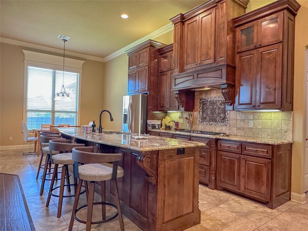 Kitchen featuring rich wood cabinetry, granite countertops, stainless steel appliances, and a tile backsplash with decorative inset