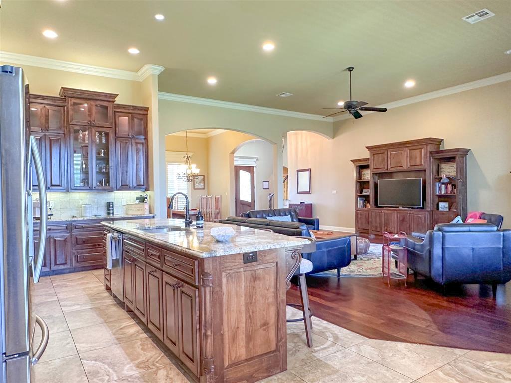 Expansive kitchen and living area featuring a large center island with a granite countertop, dark wood-finish cabinetry, recessed lighting, and a built-in entertainment center