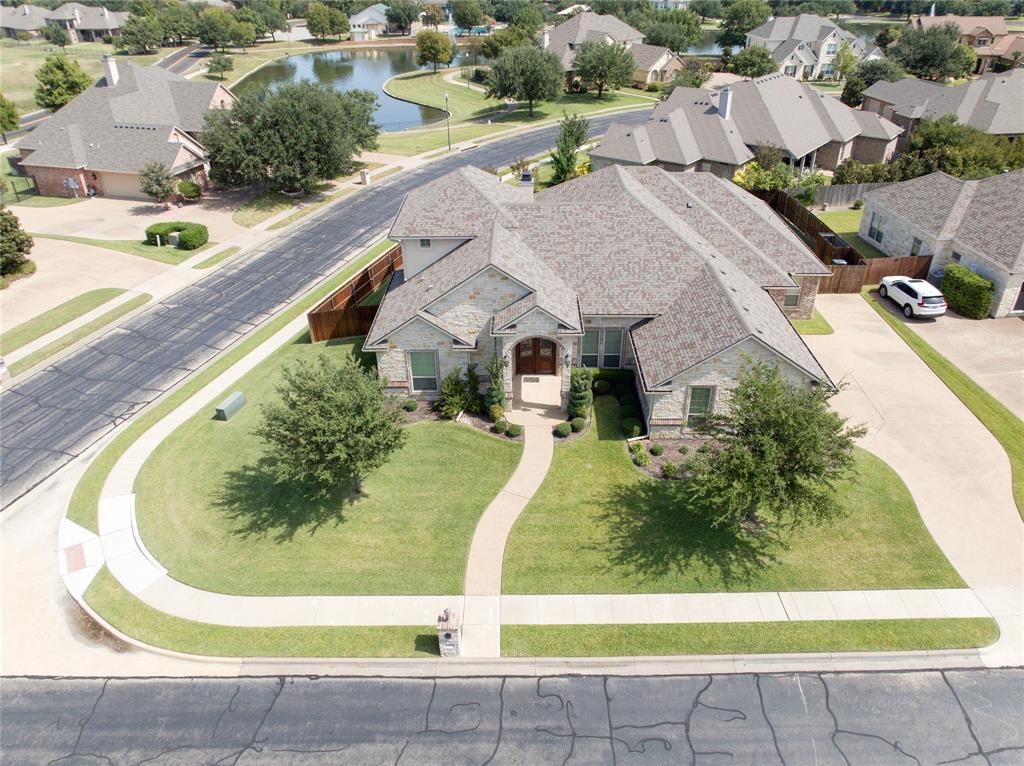 Stone-clad residence featuring a curved entry walkway, mature landscaping, a multi-gabled roofline, and an expansive driveway