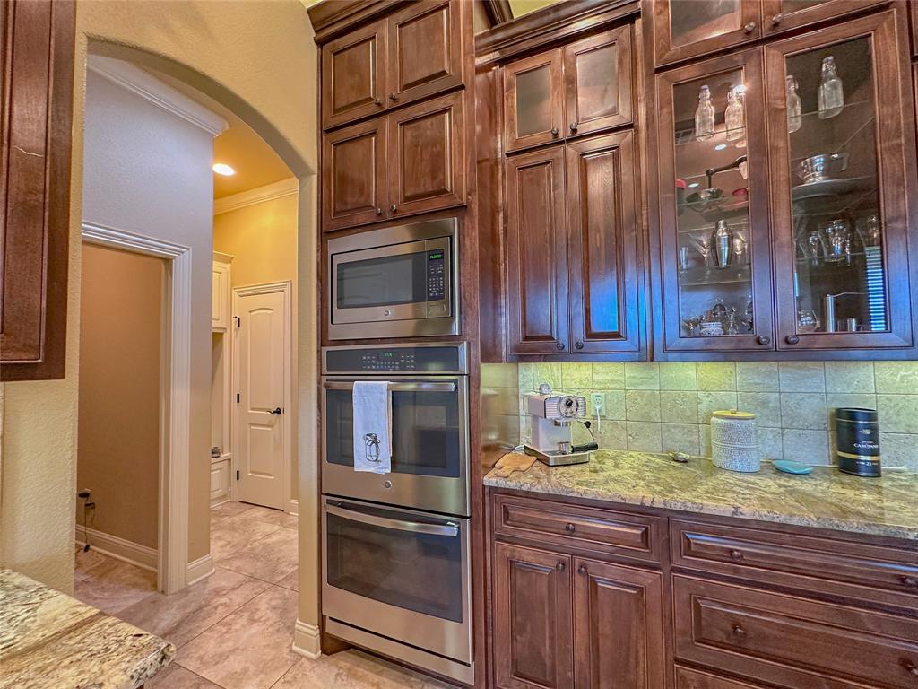 Kitchen featuring wood-finish cabinetry, stainless steel built-in microwave and oven, stone countertops, and tile backsplash