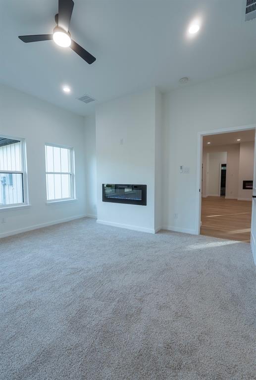Spacious room featuring plush carpeting, an integrated linear fireplace, and abundant natural light from multiple windows