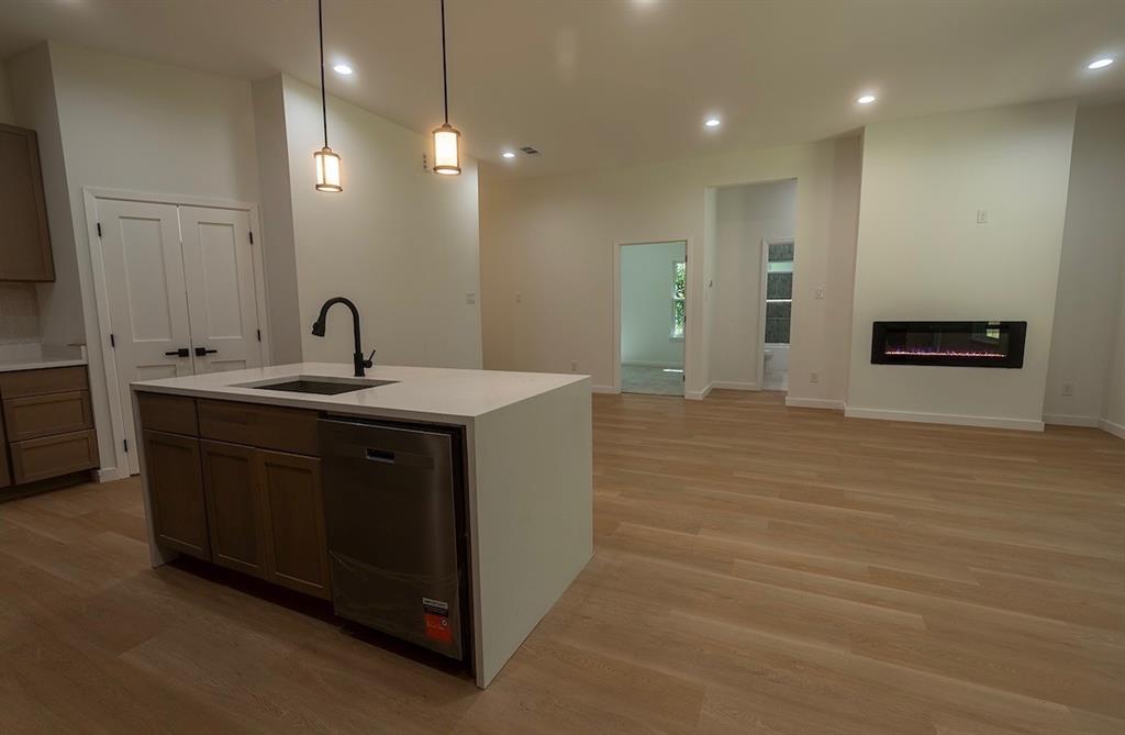 Open-concept living area featuring a kitchen island with integrated sink and dishwasher, white quartz countertops, and pendant lighting