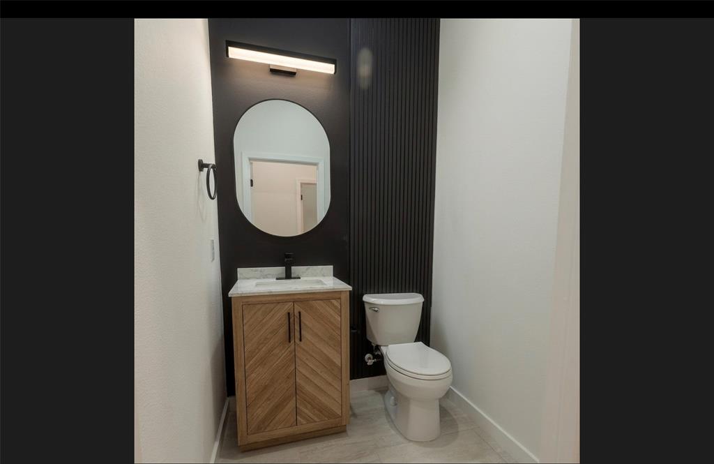 Modern powder room featuring a wood-finish vanity with chevron doors, a countertop, an oval-shaped mirror, and a sleek wall-mounted light fixture