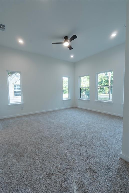 Spacious room featuring neutral carpeting, white walls, multiple windows, a ceiling fan, and recessed lighting