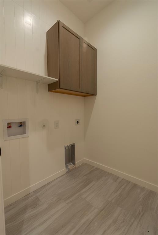 Utility room featuring wood-finish cabinetry, white shiplap wall paneling, a white shelf, and light wood-finish flooring