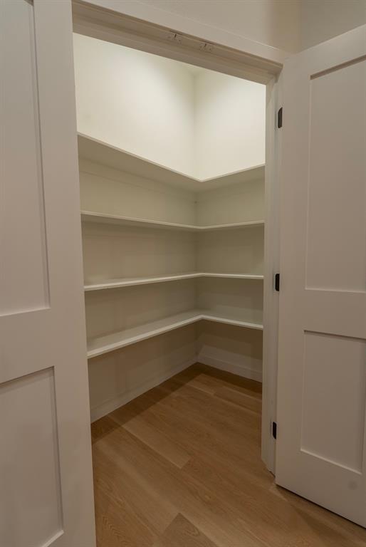 Walk-in pantry featuring light wood-finish flooring, white built-in shelving, white walls, and a recessed ceiling light