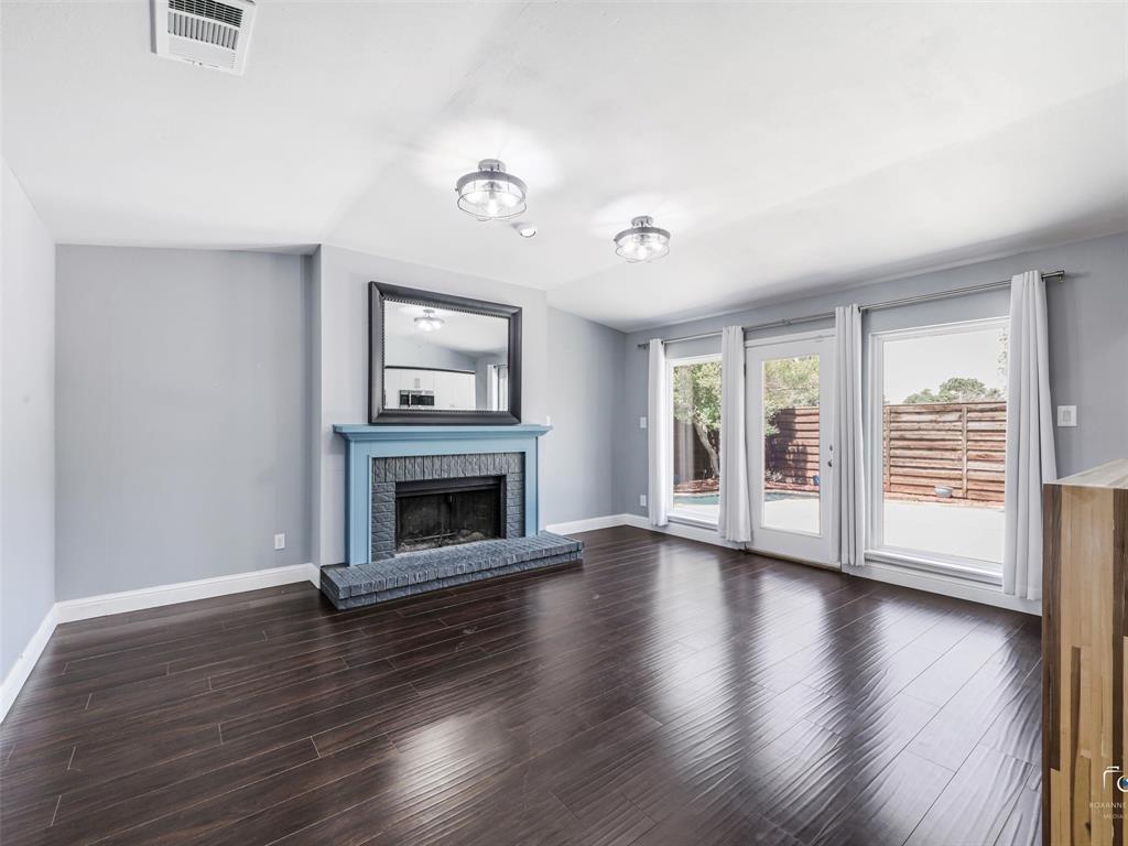 Living area featuring dark wood flooring, a fireplace with a blue mantel and dark tile surround, and two windows and a glass door opening to the backyard. Living area featuring dark wood flooring, a fireplace with a blue mantel and dark tile surround, and two windows and a glass door opening to the backyard.