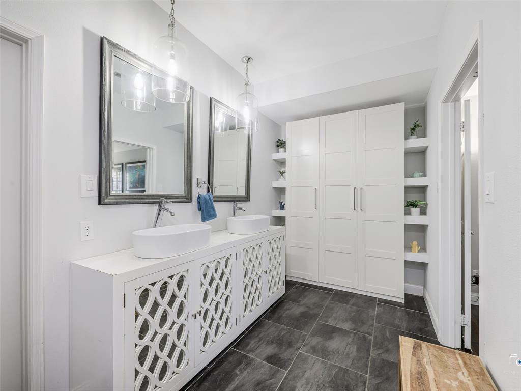 Bathroom featuring a dual vanity with vessel sinks, ornate cabinet fronts, pendant lighting, and a built-in storage unit with open shelving