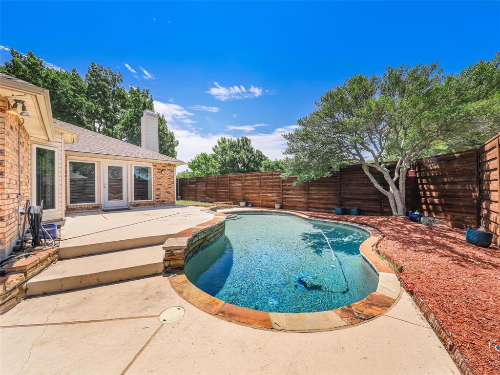 Backyard swimming pool with stone coping and an expansive concrete patio and a view of the back of the home.