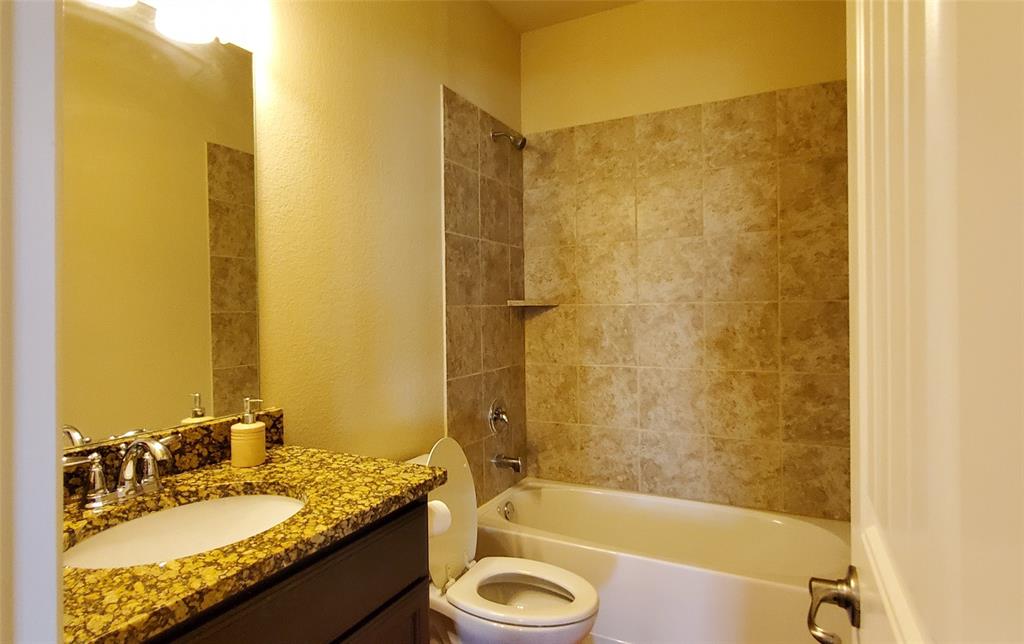 Bathroom featuring a white bathtub, ceramic tile shower surround with integrated shelf, vanity with a granite countertop, undermount sink, and chrome fixtures