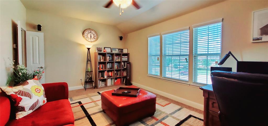Room featuring a vaulted ceiling with a ceiling fan, three windows with blinds, built-in shelving, and carpet flooring