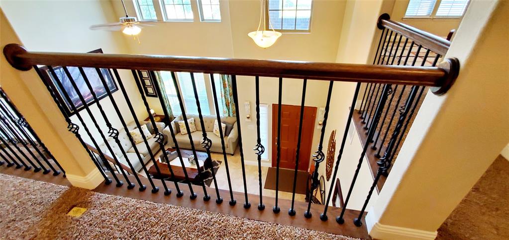 Upper-level landing featuring a wood handrail with decorative black iron balusters, overlooking a two-story foyer