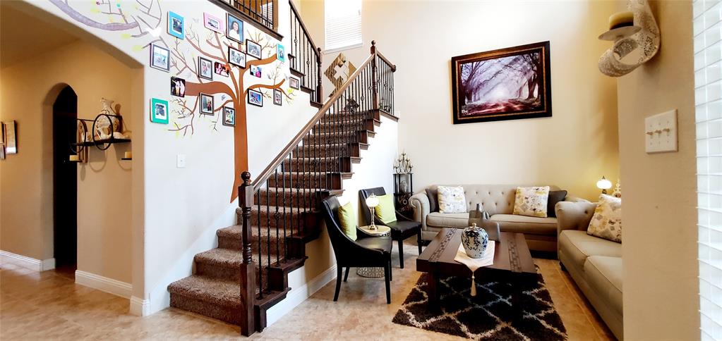 Inviting living area featuring a prominent staircase with dark wood-finish banisters and carpeted treads, alongside light-toned tile flooring
