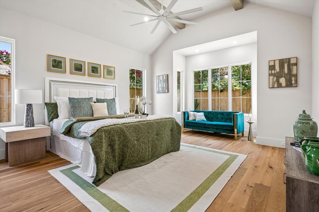 First-floor primary suite, vaulted ceiling with beams, ceiling fan, sitting area, hardwood floors