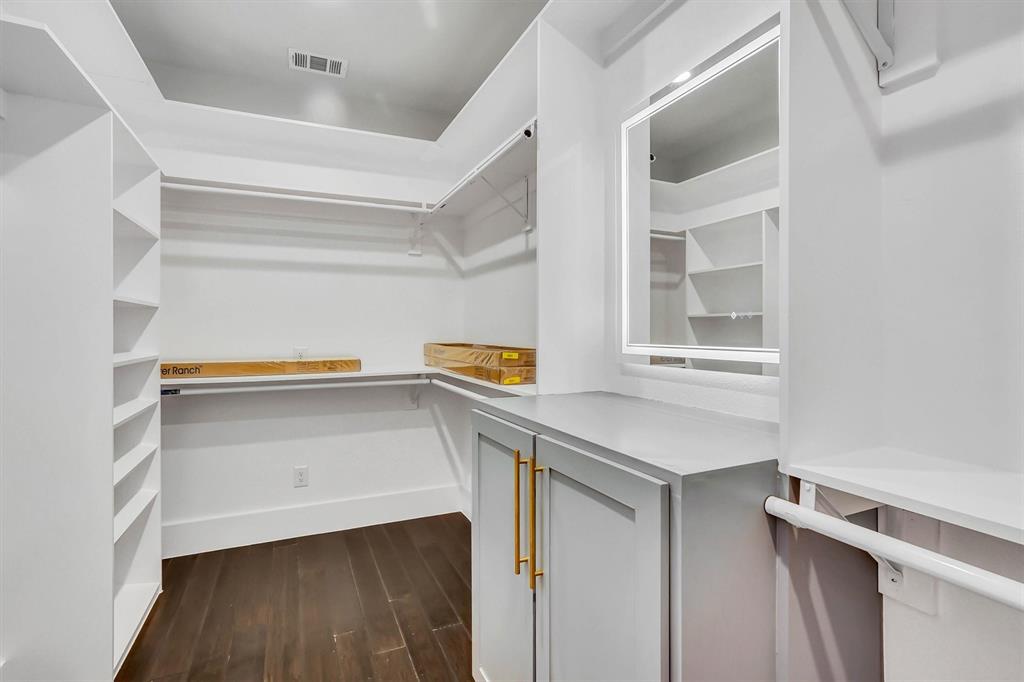 Custom closet system featuring dark wood-finish flooring, built-in shelving, hanging rods, and a central cabinet with gold-tone hardware