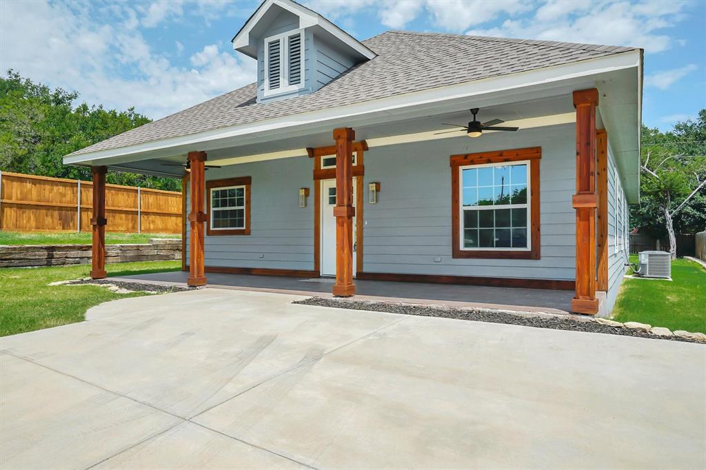 Front porch with exposed wood columns, light gray siding, a dormer with louvered shutters, and a dark shingle roof