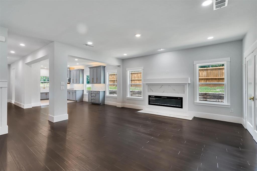 Spacious interior with dark wood-finish flooring, recessed lighting, and a modern fireplace featuring a white mantel and marble-patterned surround
