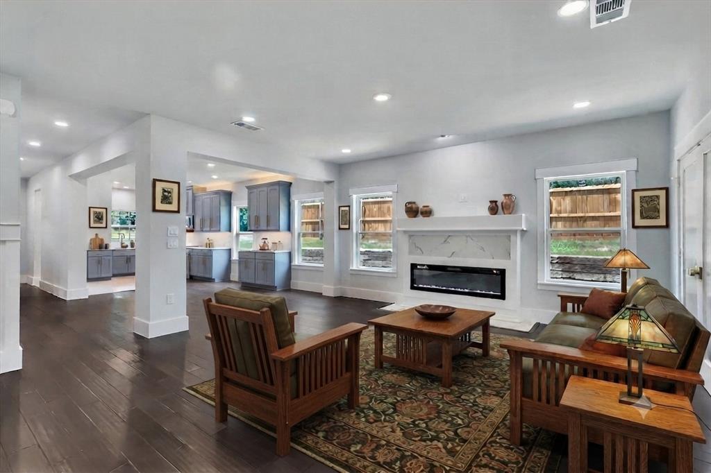 Spacious open-concept living area featuring dark wood-finish flooring, recessed lighting, and a modern fireplace with a white surround and mantel