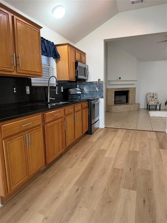 Kitchen with wood-finish flooring, wood cabinetry, dark countertops, and stainless steel appliances Kitchen with wood-finish flooring, wood cabinetry, dark countertops, and stainless steel appliances